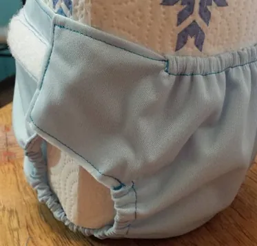 Pale blue PUL diaper cover with teal topstitching on a baby