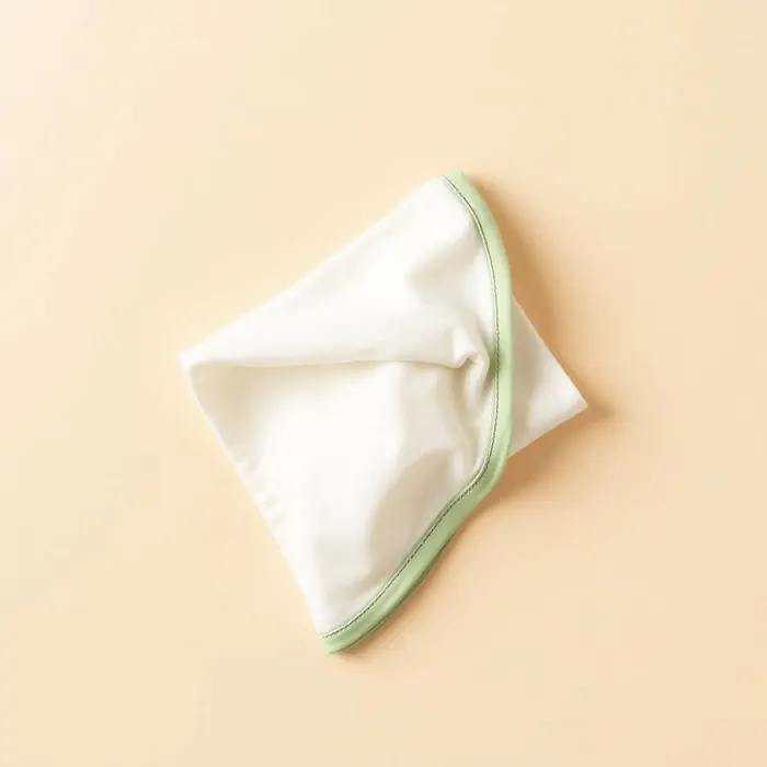 Folded cream feeding cloth with sage trim on a warm background